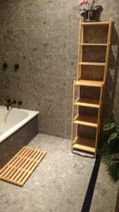 tiled bathroom area with dark tiles and light wooden shelving to contrast