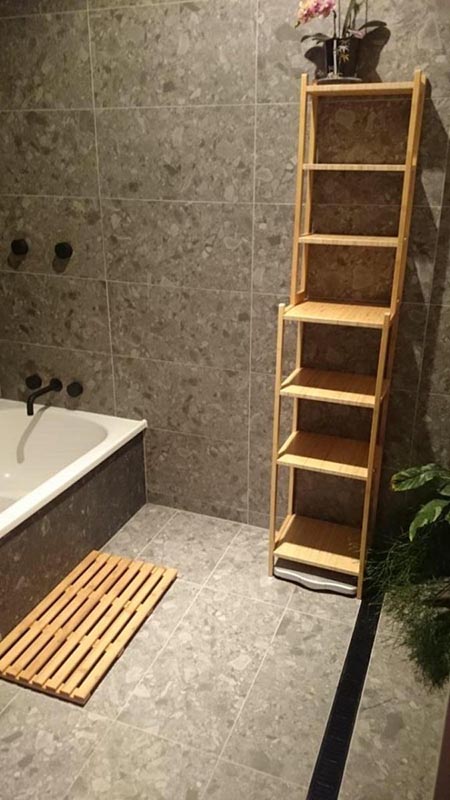 tiled bathroom area with dark tiles and light wooden shelving to contrast