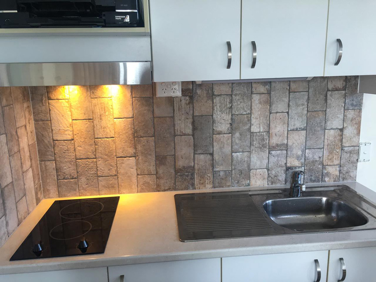 Kitchenette with sink and 2 element cook-top. Tiles are rustic brick look and tiled in a vertical brick-bond pattern.